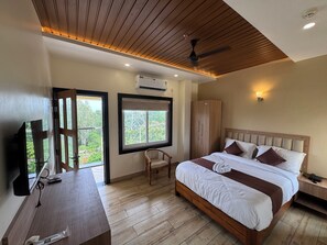 A hotel room with a bed, a desk, a wardrobe, and a window with a view of greenery.
