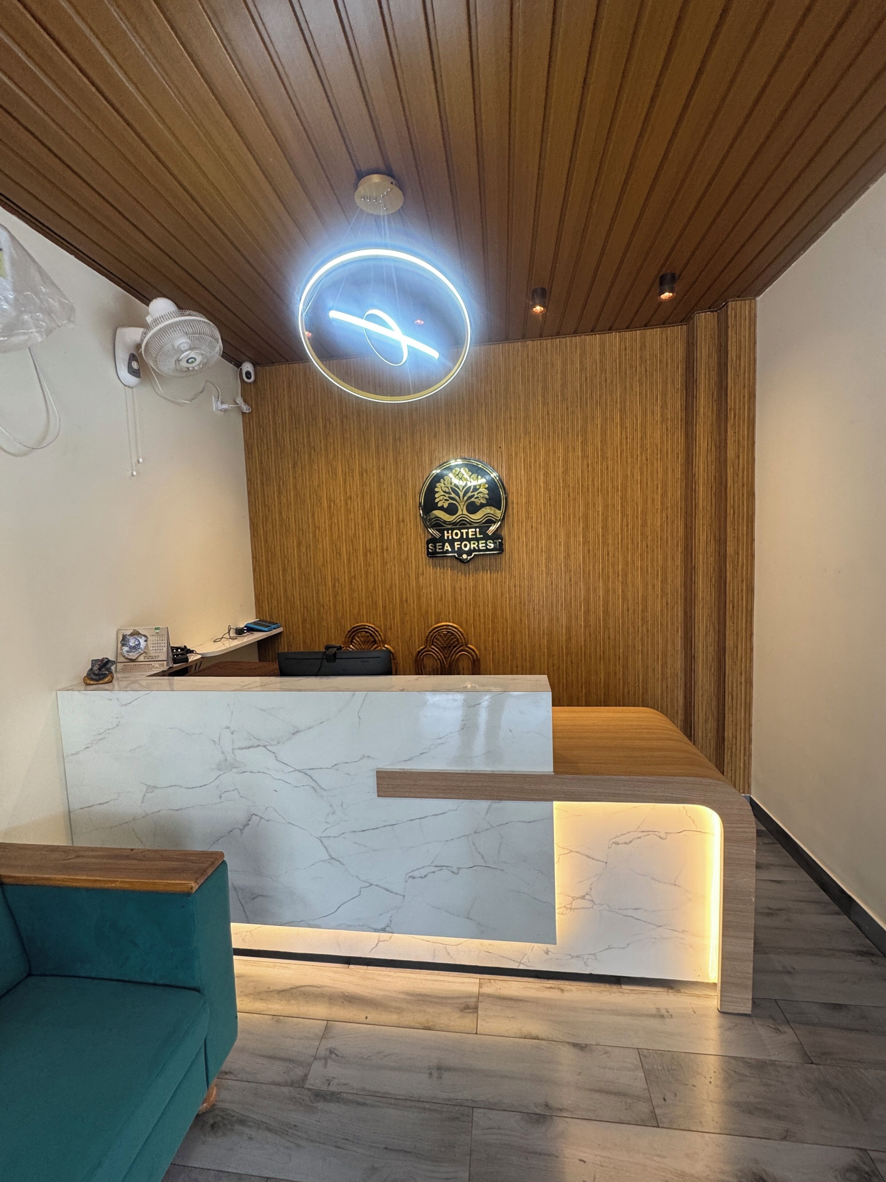 A hotel reception desk with a marble top, a wooden reception area, a neon sign, and a logo on the wall.