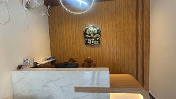 A hotel reception desk with a marble top, a wooden reception area, a neon sign, and a logo on the wall.