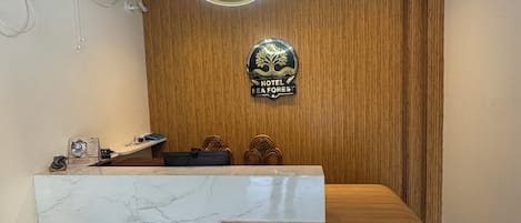 A hotel reception desk with a marble top, a wooden reception area, a neon sign, and a logo on the wall.