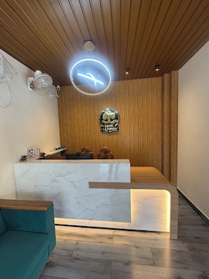 Un mostrador de recepción de hotel con encimera de mármol, zona de recepción de madera, un letrero de neón y un logotipo en la pared.