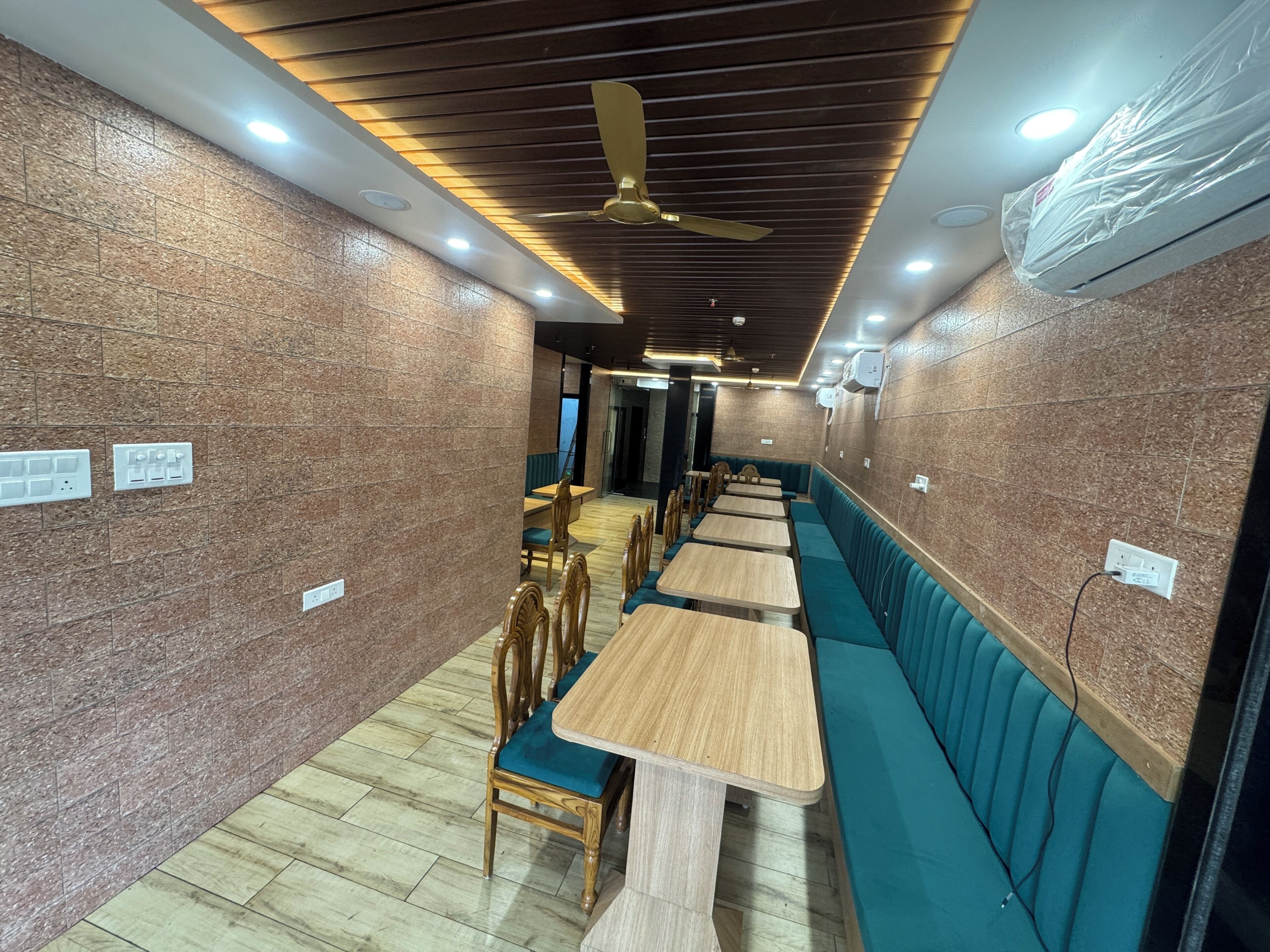 A restaurant interior with wooden tables and teal cushioned booths, ceiling fans, recessed lighting, and a brick wall.