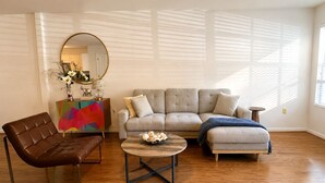 A living room with a sofa, a coffee table, and a leather chair. There is a colorful cabinet and a mirror on the wall. - Charming Town home in “La Casita” at Haile. Safe, and Close to Everything (Gainesville)