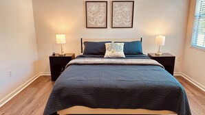 A bedroom with a bed, two bedside tables, two wall-mounted lamps, and two framed floral wall art pieces. - Charming Town home in “La Casita” at Haile. Safe, and Close to Everything (Gainesville)