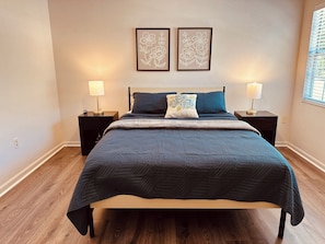 Un dormitorio con una cama, dos mesitas de noche, dos lámparas de pared y dos cuadros con motivos florales.