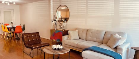 A living room with a brown leather sofa, a round coffee table, a beige sectional sofa, and a dining area with a table and colorful chairs.
