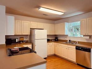 Cocina con armarios blancos, refrigerador, microondas, lavavajillas y ventana con vista a follaje.