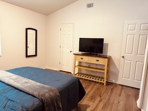 A bedroom with a bed, a TV on a wooden stand, and two doors.