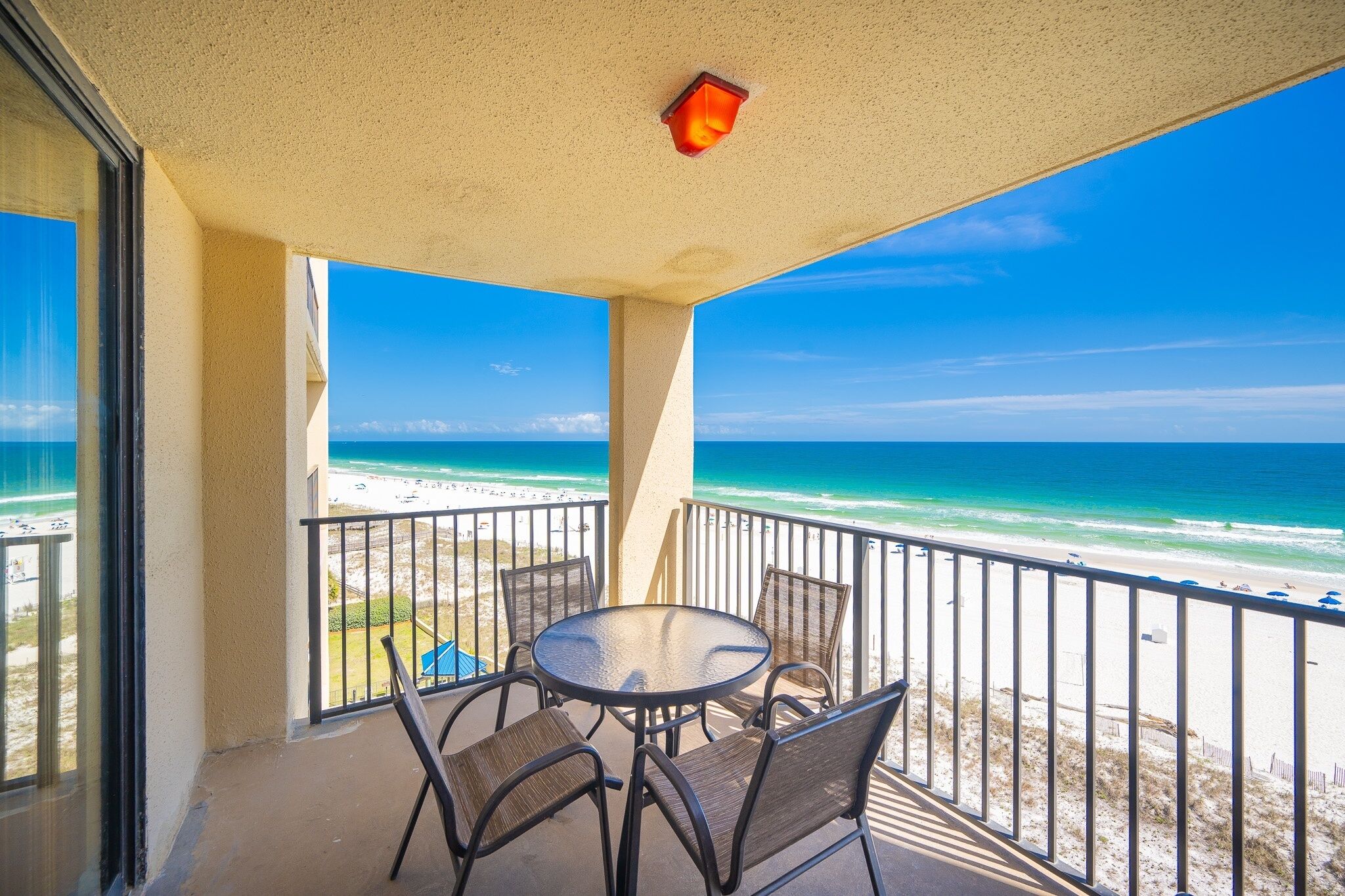 A balcony with a table and chairs, overlooking a beach with a clear view of the ocean.