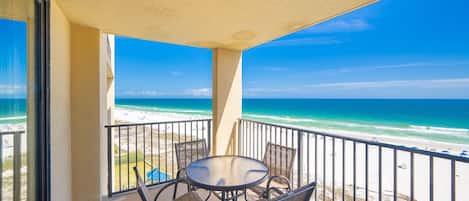 A balcony with a table and chairs, overlooking a beach with a clear view of the ocean.