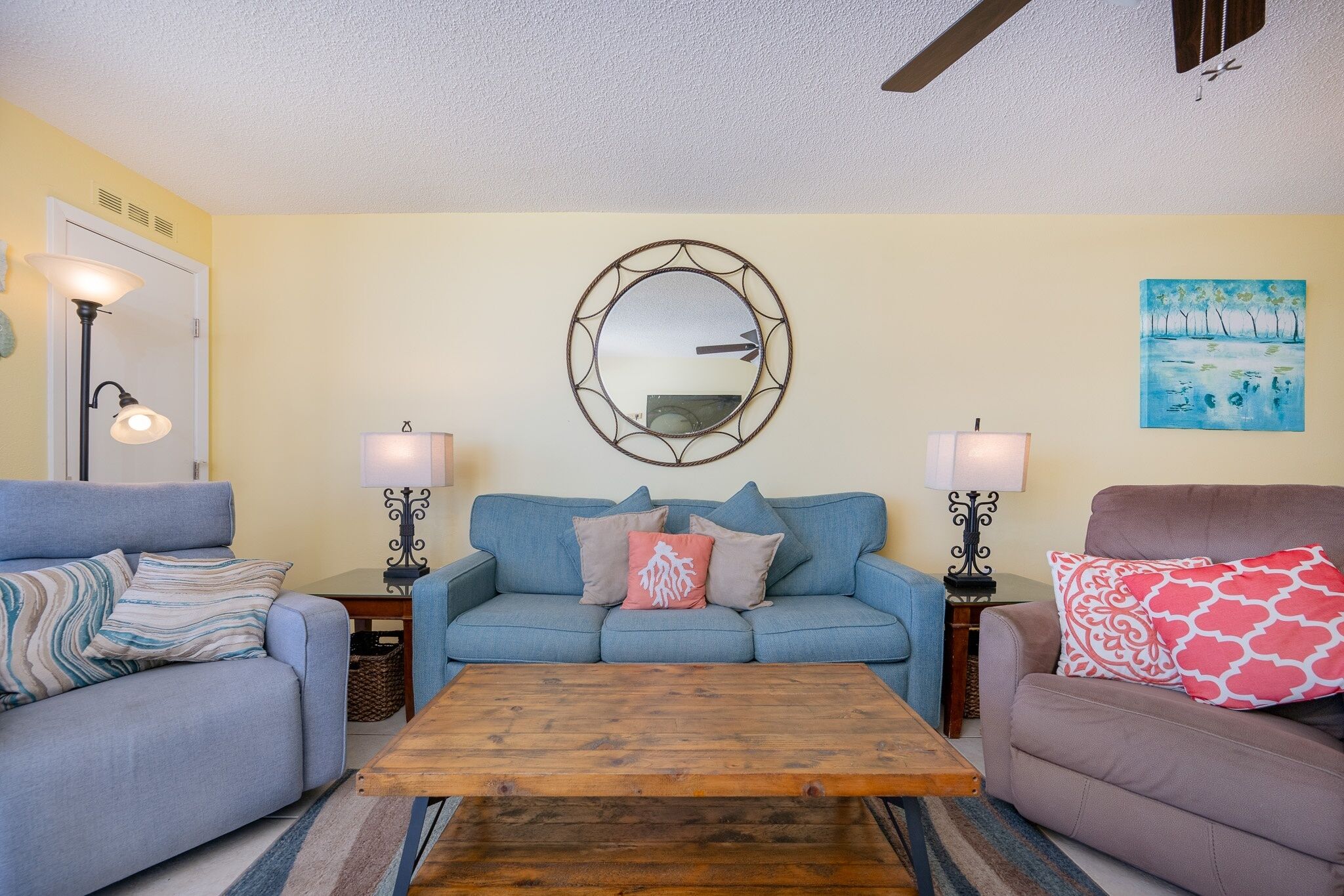 A living room with a blue sofa, two side tables with lamps, a wooden coffee table, and a wall-mounted mirror.
