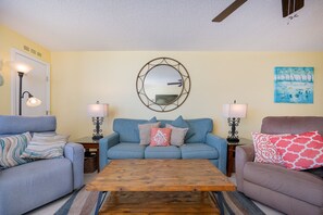 Ein Wohnzimmer mit einem blauen Sofa, zwei Beistelltischen mit Lampen, einem Holztisch und einem an der Wand befestigten Spiegel.