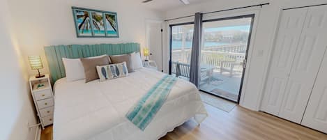 A bedroom with a bed, a nightstand, a ceiling fan, a window with a view of a balcony, and a door.
