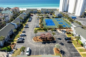 An aerial view of a parking lot with a tennis court, surrounded by residential buildings and a beach. - South Bay By The Gulf 054 2 Bedroom Townhouse (Destin)