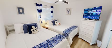 Une chambre avec deux lits, un ventilateur de plafond, une télévision et une commode.