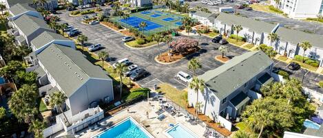 Vista aérea de un hotel con varias construcciones, estacionamiento, cancha de tenis, piscina y vistas a la playa.