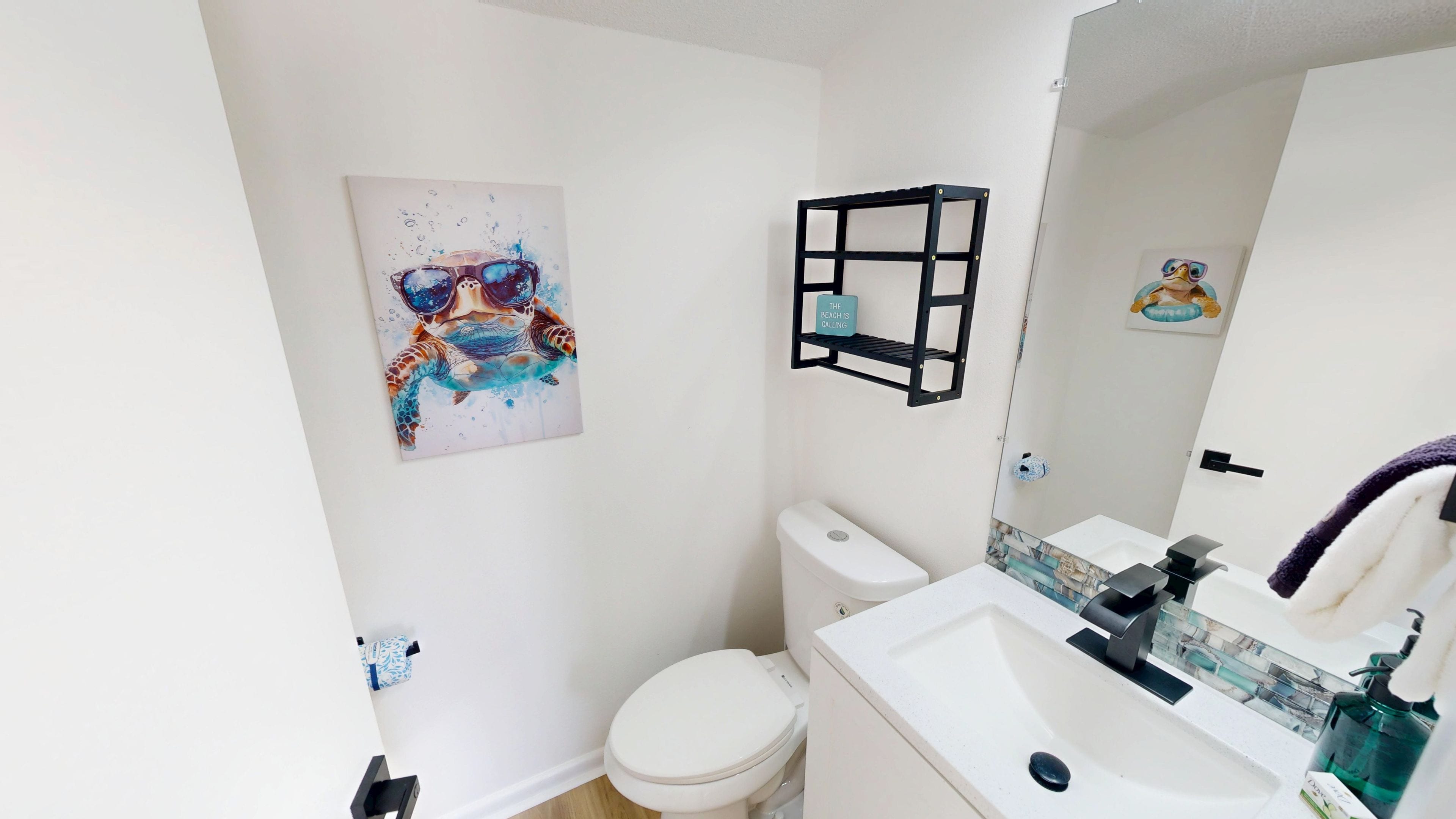 A bathroom with a toilet, sink, mirror, and a wall-mounted shelf with a sign.