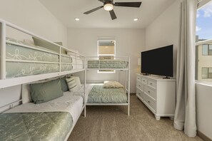 Quarto com beliches, televisão, cômoda e ventoinha no teto.