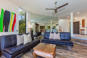 A modern living room with two black leather sofas, a glass coffee table, and a ceiling fan. - Wailea Ekahi 3a 2 Bedroom Condo (Kihei)