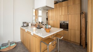 A modern kitchen with wooden cabinets, a central island with stools, a built-in oven, and various kitchen utensils. - Holiday Home 'Casa Opala Townhouse with Pool' , Wi-Fi and Air Conditioning (Olhão)