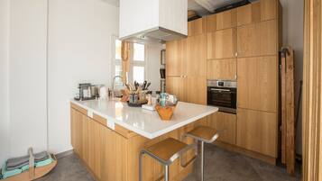 A modern kitchen with wooden cabinets, a central island with stools, a built-in oven, and various kitchen utensils.