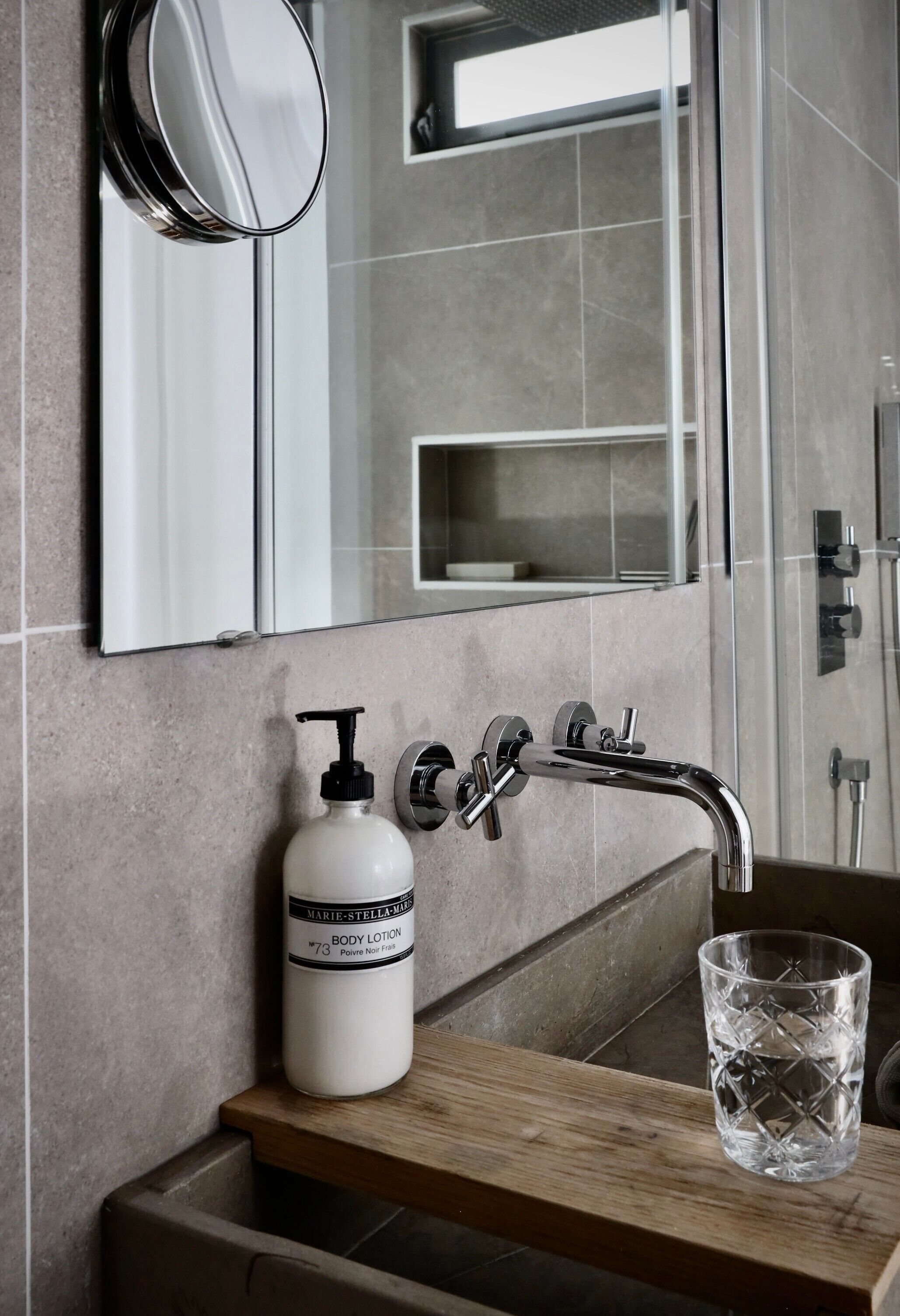 Un baño con espejo, un lavabo con dispensador de jabón y un vaso de agua en la encimera.