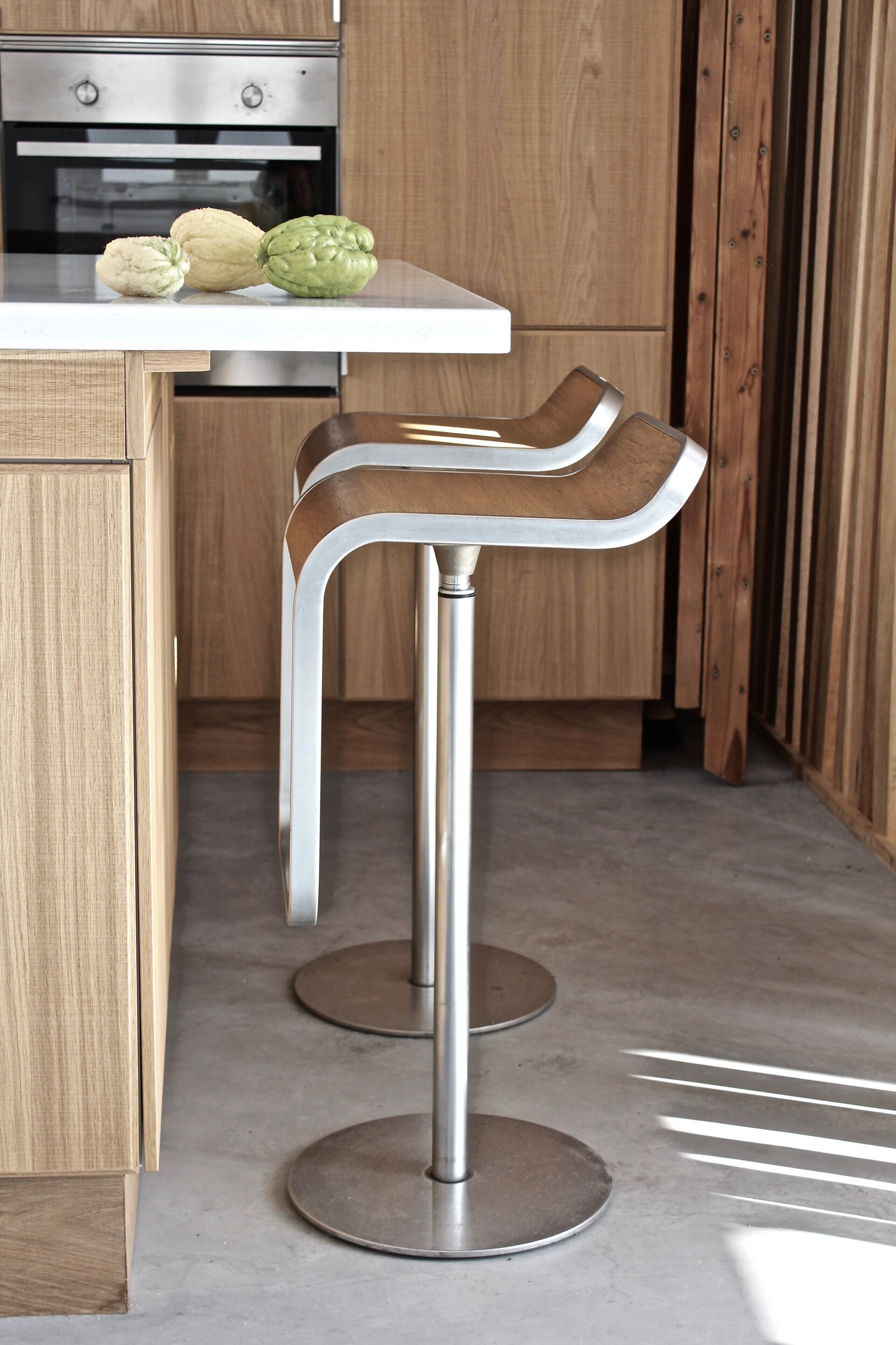 A kitchen with a white countertop, two stainless steel bar stools, and a wooden cabinet.