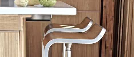 Une cuisine dotée d’un plan de travail blanc, de deux tabourets de bar en acier inoxydable et d’un meuble en bois.