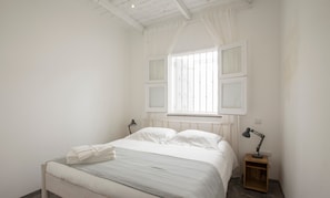 Une chambre à coucher avec un lit, une fenêtre avec des rideaux, une table de chevet avec une lampe et un radiateur.