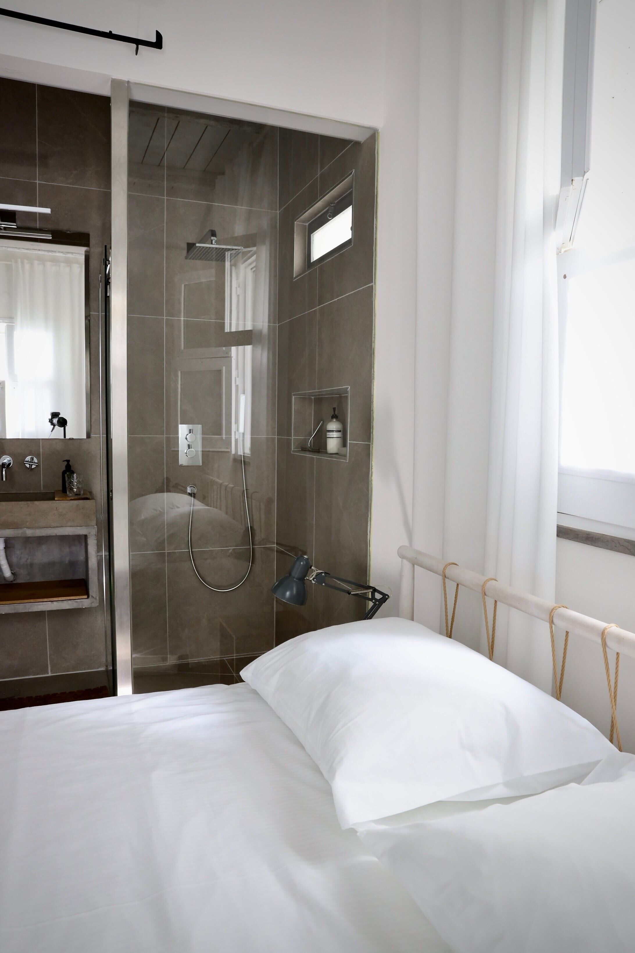 Une salle de bain moderne avec une douche à parois de verre, un lavabo intégré et une table de chevet avec une bouteille.