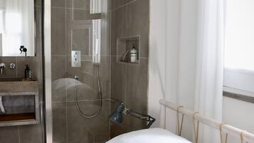 Une salle de bain moderne avec une douche à parois de verre, un lavabo intégré et une table de chevet avec une bouteille.