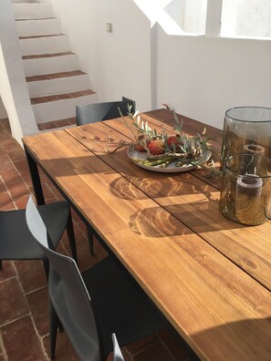 Une table à manger en bois, avec des chaises, une assiette de nourriture et un porte-bougie en verre.