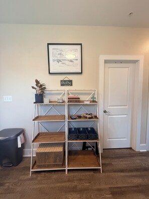 A room with a white door, a framed picture on the wall, a shelf with various items, and a trash bin. - Salt & Serenity on 30A Walk to Santa Rosa Beach! 
CLEAN, 1st Floor Unit (Santa Rosa Beach,)