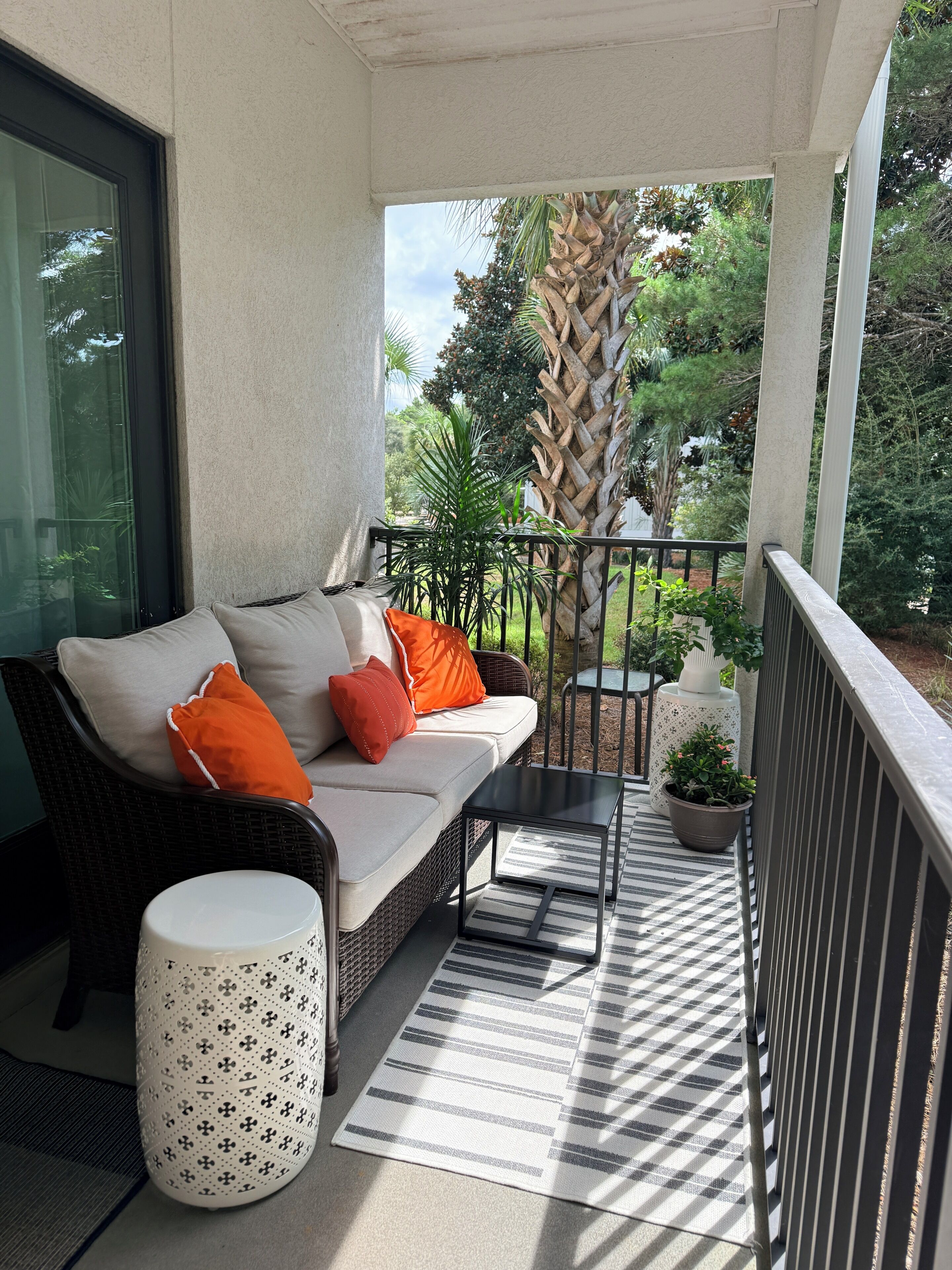 A balcony with a wicker sofa, a small round table, and a potted plant.