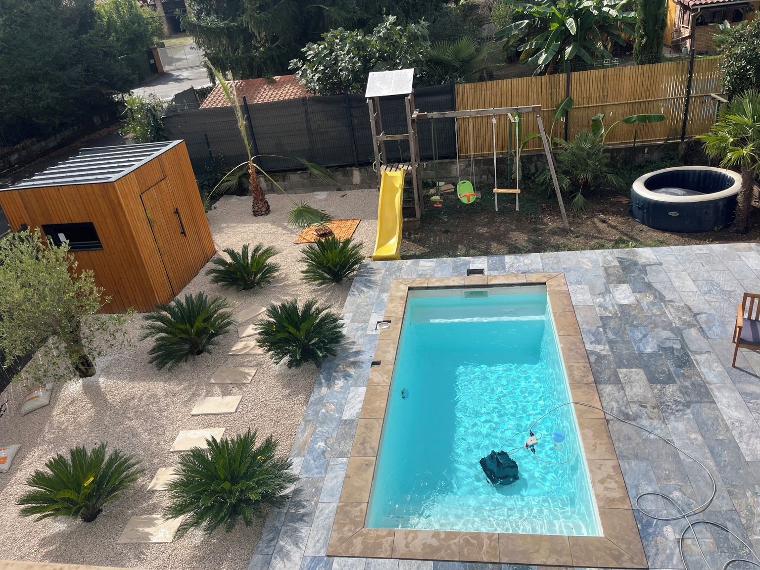 Une piscine dotée d’une terrasse carrelée, entourée de plantes en pot et d’une structure en bois.