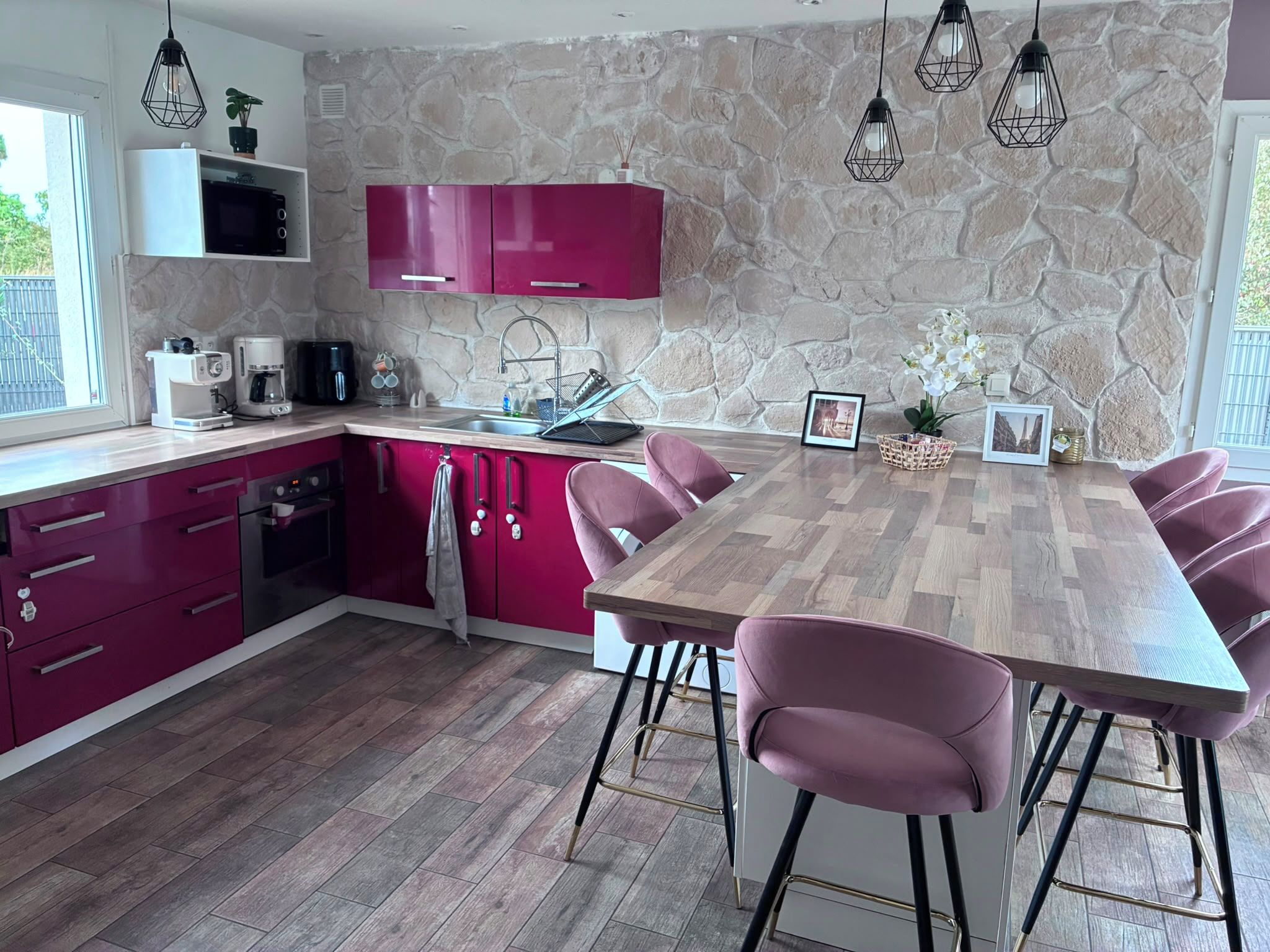Eine moderne Küche mit rosa Schränken, einem Holztisch und Barhocker.