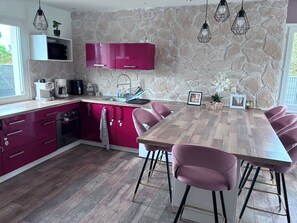 A modern kitchen with pink cabinets, a wooden dining table, and bar stools.