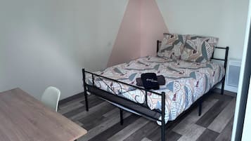 A single bed with a patterned bedspread, a small table, and a chair in a room with a sloped ceiling and a radiator.