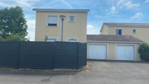 A two-story building with a garage door and a black fence in the foreground. - The Sunny House (Bérat)