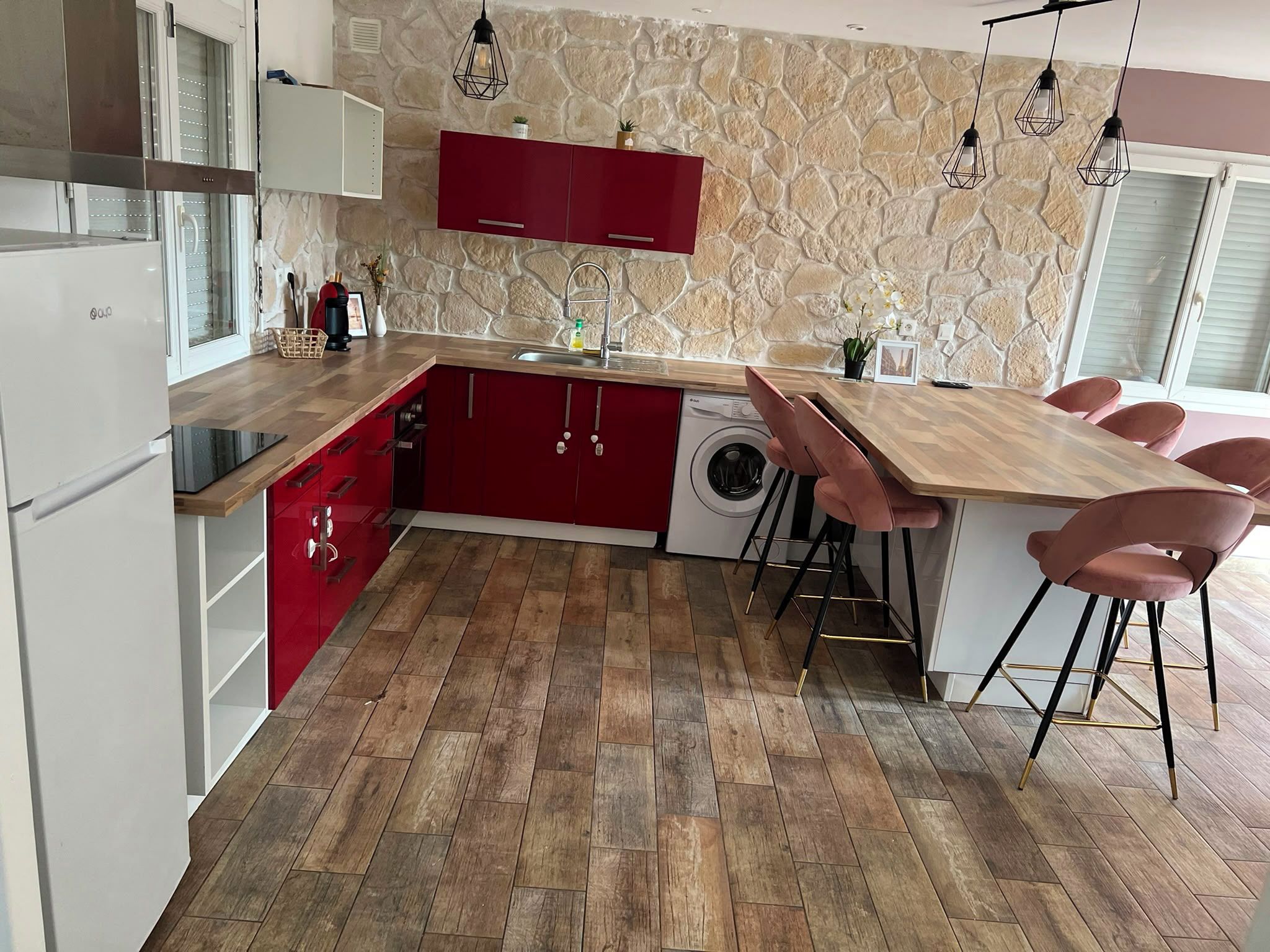 Cocina moderna con salpicadero de pared de piedra, armarios rojos, encimera de madera y lavadora integrada.