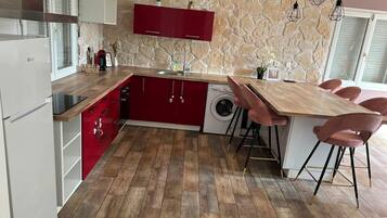 Cocina moderna con salpicadero de pared de piedra, armarios rojos, encimera de madera y lavadora integrada.