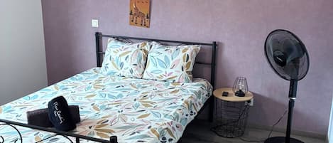 Un dormitorio con una cama, un ventilador, una mesita de noche con una lámpara y dos adornos en la pared.