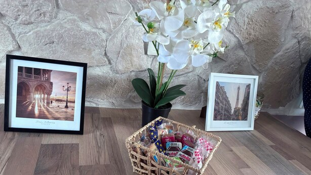 A wooden floor with framed pictures, a potted plant, and a basket of items. - The Sunny House (Bérat)