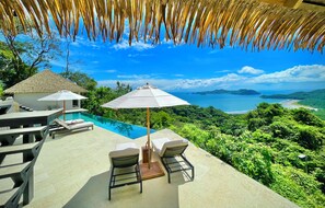 A poolside area with lounge chairs and umbrellas, overlooking a scenic ocean view.