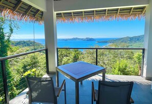 A balcony with a table and chairs overlooking a scenic view of the sea and hills.