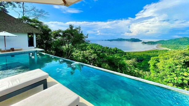 Une magnifique piscine à débordement d’un bleu profond, offrant une vue sur une plage et une végétation luxuriante.
