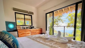 Une chambre avec un grand lit, une commode en bois, un miroir et une vue sur l’extérieur grâce à une porte-fenêtre coulissante.