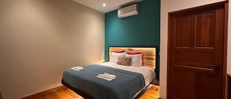 A bedroom with a bed, a ceiling fan, an air conditioning unit, and a wooden door.