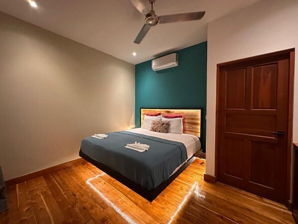 A bedroom with a bed, a ceiling fan, an air conditioning unit, and a wooden door.