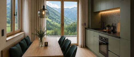 A modern kitchen with a dining area, large windows, and a view of mountains.
